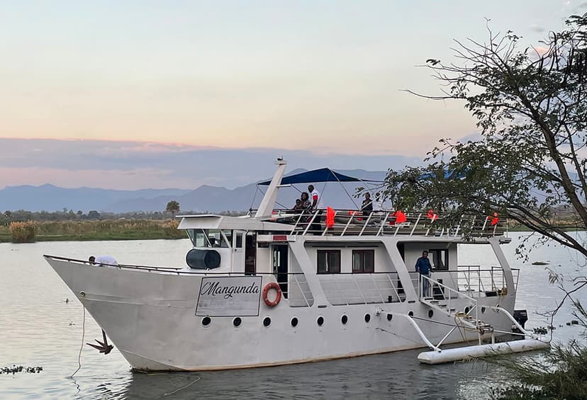 White cruise boat docked on calm waters at sunset with passengers on deck enjoying the tranquil view.