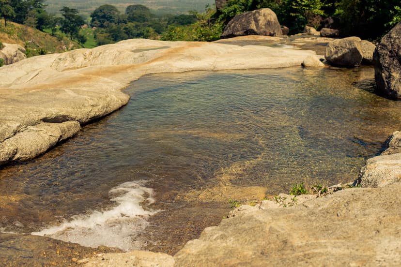 Clear natural pool surrounded by smooth rocks and greenery, perfect for a refreshing outdoor dip.