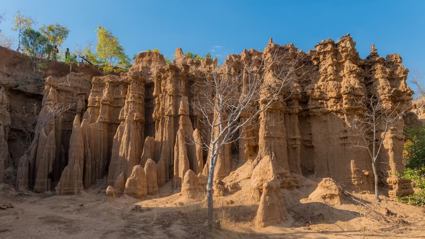 Majestic natural rock formations with tall, sculpted pillars and rugged terrain under clear blue skies.