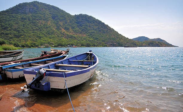Wooden fishing boats docked by the shore of Lake Malawi with mountains in background